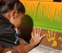 young Native American child leaves her handprint on a large outdoor mural