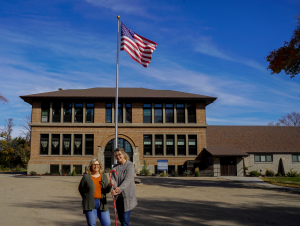 Chris Armbrust and Teresa Perleberg holding a shepherd's crook in front of the newly renovated Nome Schoolhouse