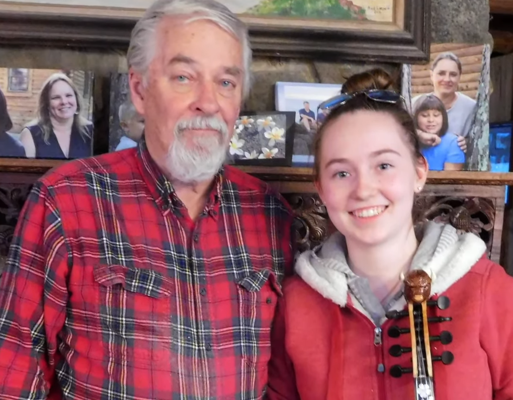 Master Hardanger fiddle maker and player Bud Larson standing next to his teenage apprentice Ruth Dramstad of Cass County, holding a fiddle and smiling