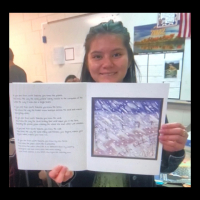 Williston High School student holding their art and writing booklets up to the monitor during Zoom class