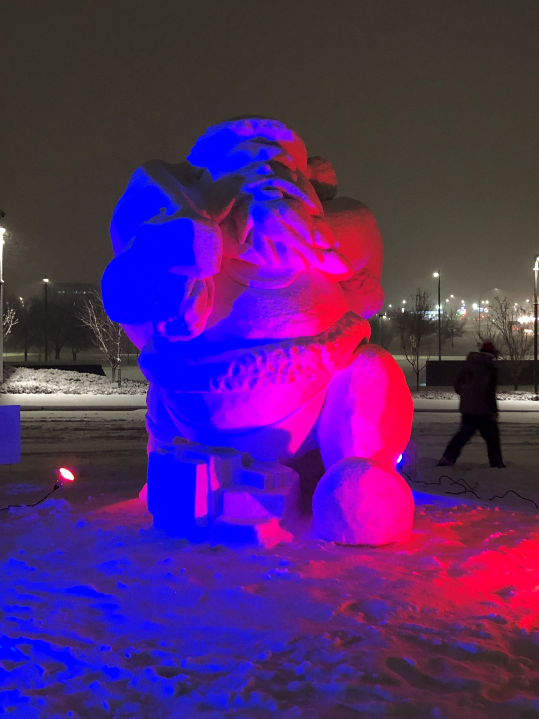 Large Santa Claus snow sculpture with blue and pink lights projected onto it