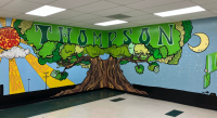 Colorfully painted mural of a huge tree in the center with a sun and rays on the left and a half moon on the right - on two walls in the cafeteria at Thompson Public School; &quot;THOMPSON&quot; in all caps at the top of the tree, inside the leaves; with inspirational words written in the rays, including: determination, faith, adaptable, community, teamwork, grit, collaboration, character, kindness, intelligence, openness, empathy, respect, unity, patience and compassion
