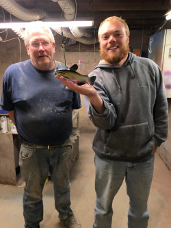 Rick Whittier standing in a large shop area next to Walker Bruns who is holding a colorful spearfish decoy