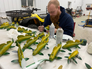 Walker Bruns sitting at a table, making many fish decoys