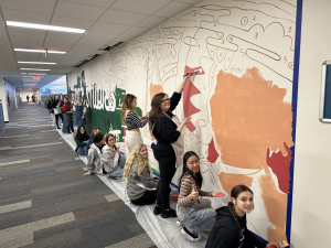 Students at Watford City High School are painting a 20 foot by 10 foot mural (by number) that contains abstract images, including the words SOCIAL STUDIES in bright white on top of a dark background