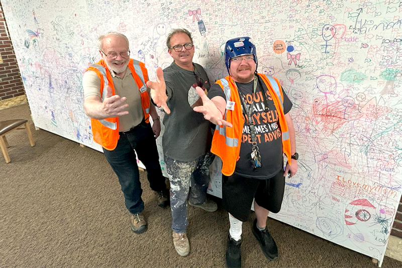 Grand Forks Children's Museum Accessibility Welcome Wall with 3 disable people standing in front, holding out their hand in welcome