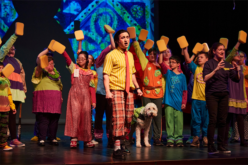Colorful cast of various races, ages, and abilities in The SpongeBob Musical inhabit the stage in all their glory with neurodiverse SpongeBob and Deaf Patrick Star gesturing grandly with arms open. Photo Credit: Jeff Heimbach