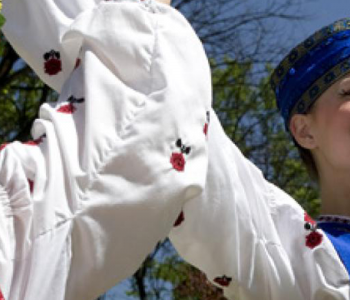Young girls wearing bright Ukrainian costumes with puffy white sleeves and hats, smiling and dancing with their arms in the air